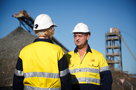 Redpath employees having a discussion in front of surface level industrial mining structures.